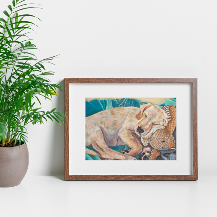 A mockup of the young puppy image in a mount and frame next to a lush green plant. 